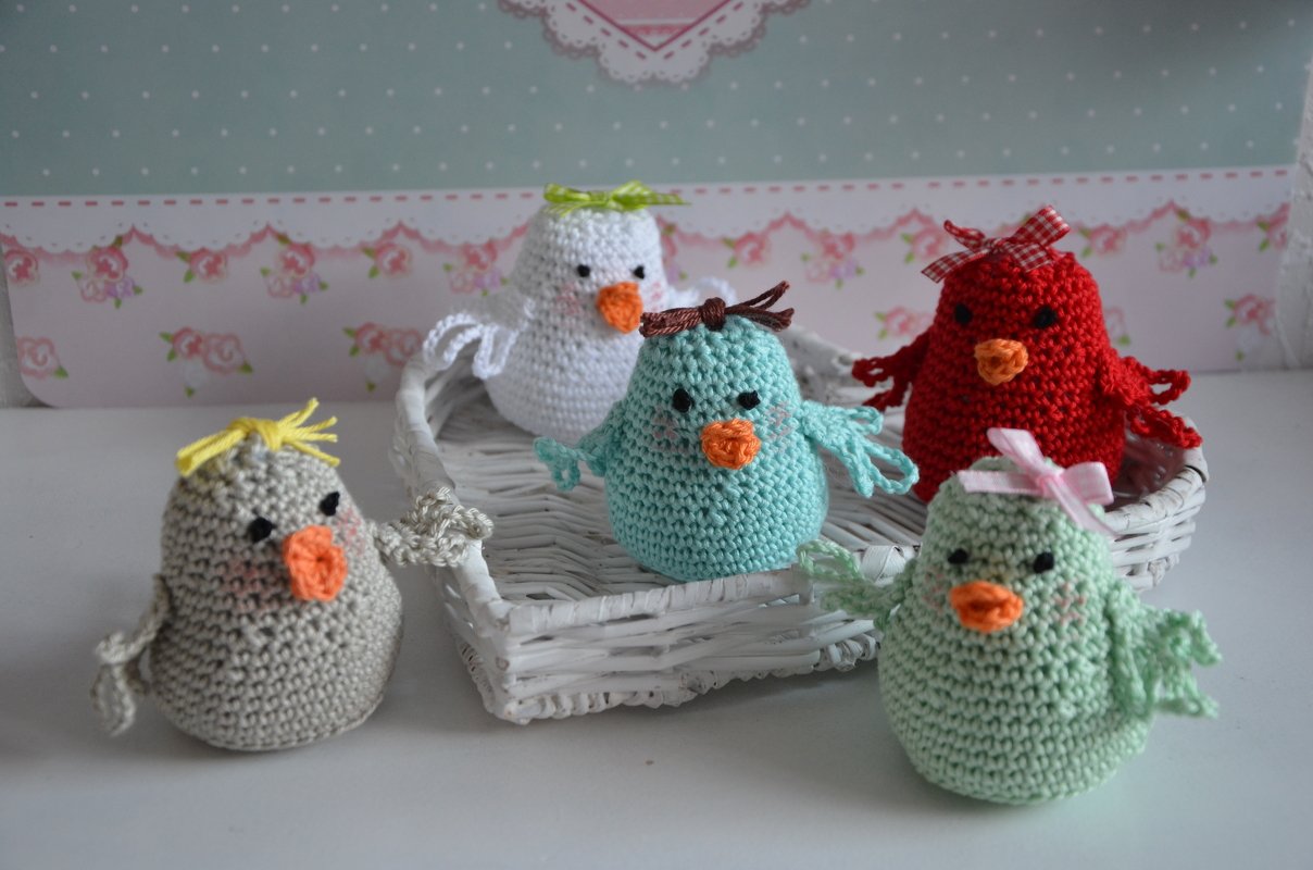 Fünf gehäkelte Amigurumi‑Vögel in Weiß, Blau, Rot, Mint und Grau, einige in einem weißen Korb