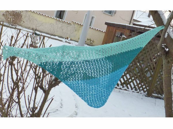 Türkis‑blaues gehäkeltes Dreieckstuch im Schnee an Strauch und Baum aufgehängt