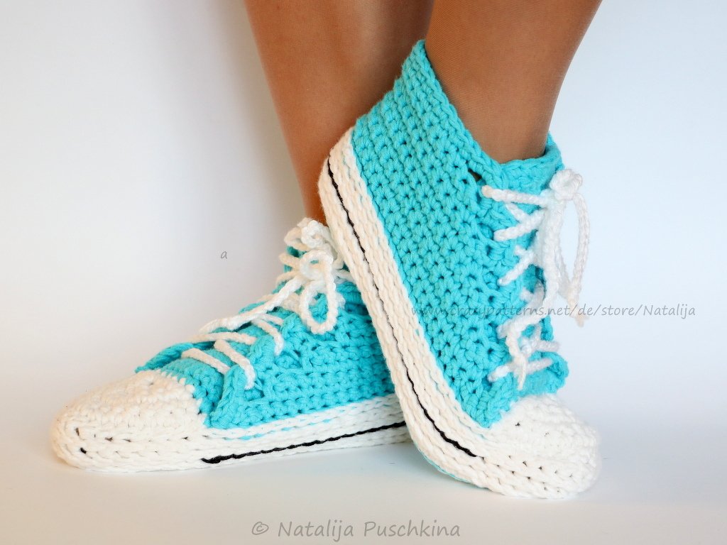 Gehäkelte türkis-weiße High-Top-Hausschuhe mit weißen Schnürsenkeln an den Füßen