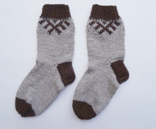 Zwei handgestrickte Socken in Hellgrau mit dunkelbrauner Ferse, Spitze und Bündchen und geometrischem Muster am Schaft.