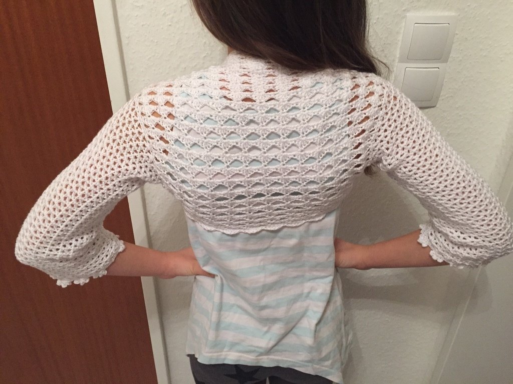 Rückenansicht einer Person mit einem weißen, gehäkelten Bolero mit Lochmuster und Drei-viertel-Ärmeln.