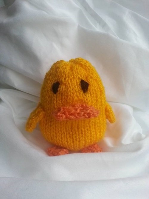 Gestricktes gelbes Küken mit orangefarbenem Schnabel und Füßen auf weißem Stoff