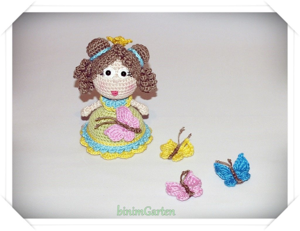 Gehäkelte Amigurumi-Puppe mit drei gehäkelten Schmetterlingen vor weißem Hintergrund