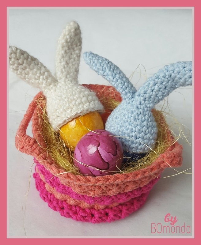 Gehäkelte Hasen-Eierwärmer (weiß, hellblau) in pink-koralle Häkelkorb mit bunten Ostereiern und Stroh