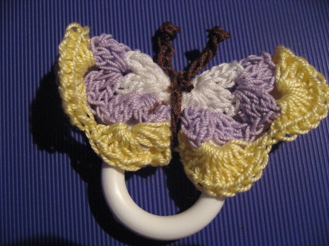 Gehäkelter Schmetterling in Gelb und Flieder an weißem Ring auf blauem Hintergrund