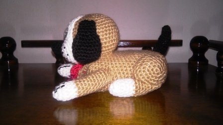 Amigurumi liegender Hund, beiger Körper, weiße Pfoten, schwarze Ohren, schwarzer Schwanz, rotes Halsband