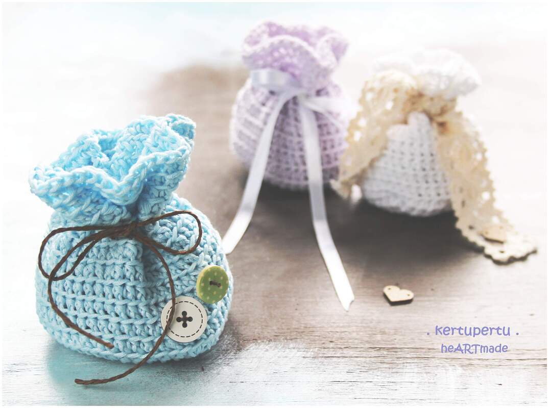 Drei gehäkelte Beutel in Hellblau, Lila und Cremeweiß mit Bändern und Knöpfen auf Holz