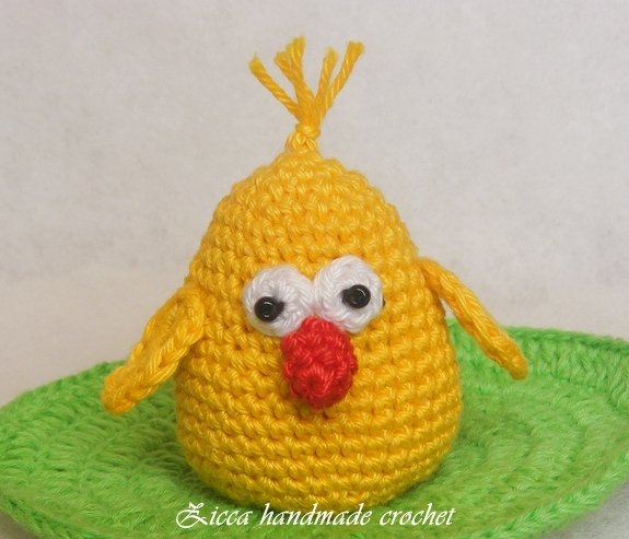 Handmade yellow crochet chick with white eye patches, red beak and top tuft on a green crocheted base