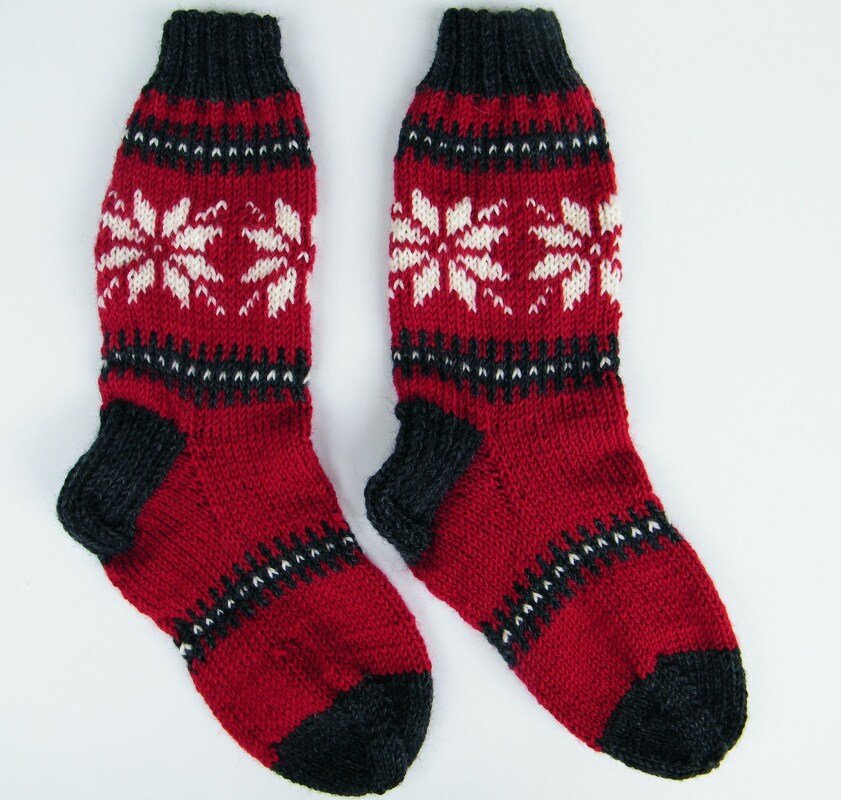 Rote gestrickte Herrensocken mit weißem Schneeflockenmuster und dunklen Fersen, Spitzen und Bündchen.