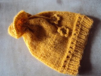 gelbe Babymütze gestrickt mit geripptem Rand, Blütenapplikationen und Rüschenabschluss