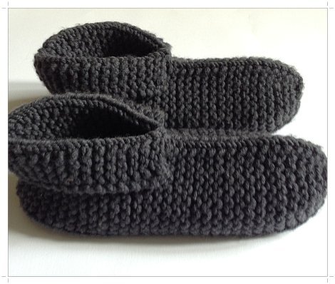 Ein Paar dunkelgraue, handgestrickte Hausschuhe aus Garn, nebeneinander auf hellem Untergrund.