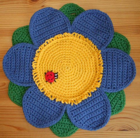 Gehäkelter Blumen-Topflappen (blau, gelb, grün) mit rotem Marienkäfer auf Holzuntergrund