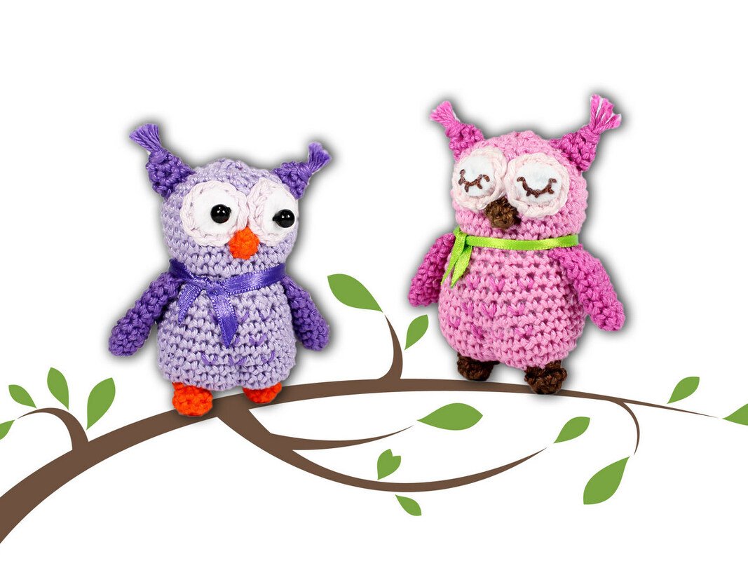 Zwei gehäkelte Amigurumi-Eulen (lila und rosa) auf einem stilisierten Zweig