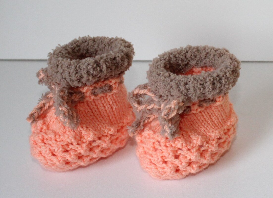Detailaufnahme von gestrickten Babyschuhen in Pfirsich und Braun mit Zierbändern
