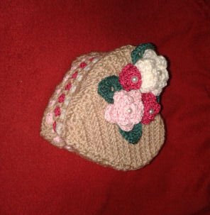 Beiges gehäkeltes Herz-Utensilo mit rosa, pinken und weißen Blumen und Perlen auf rotem Stoff