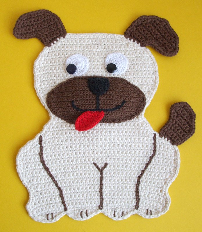 Gehäkelter Topflappen in Form eines sitzenden Hundes, cremefarben mit braunen Ohren, Schnauze und roter Zunge auf gelbem Hintergrund