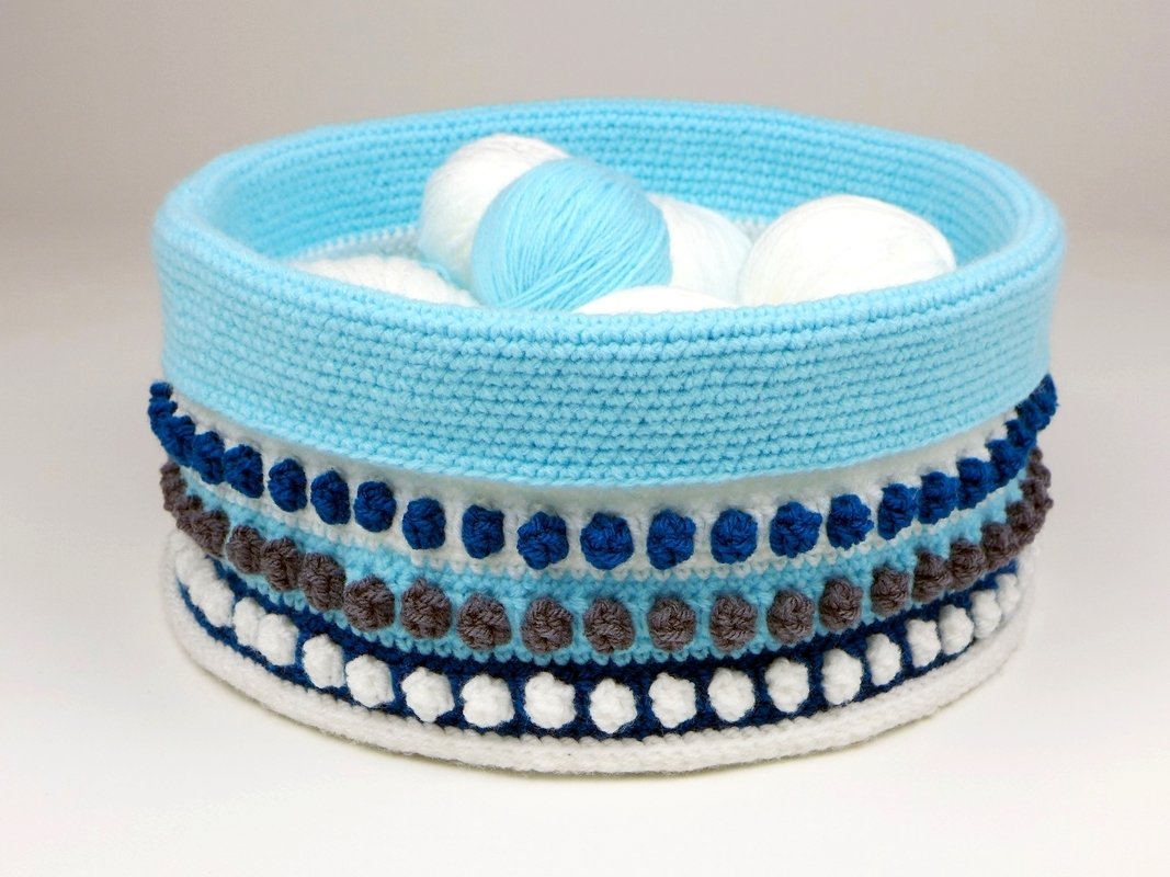 Runder gehäkelter Utensilo-Korb mit Noppenmuster in Blau, Weiß und Braun, gefüllt mit Garnknäueln
