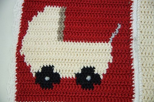 Gehäkeltes Granny Square in Rot mit cremefarbenem Kinderwagen-Motiv und schwarzen Rädern