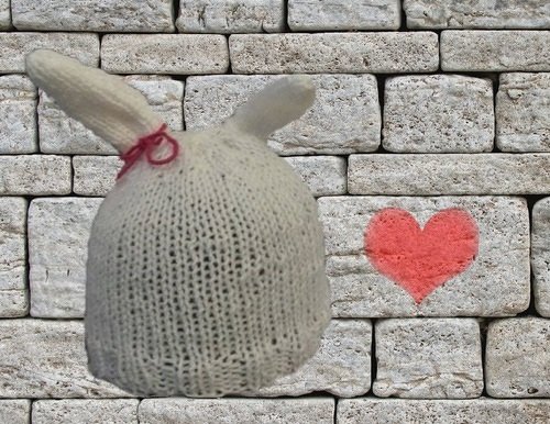 Weiße gestrickte Babymütze mit Hasenohren und roter Schleife