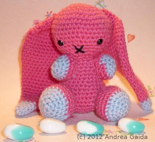 Rosa gehäkelter Amigurumi‑Hase mit Schlappohren und hellblauen Pfoten, sitzend