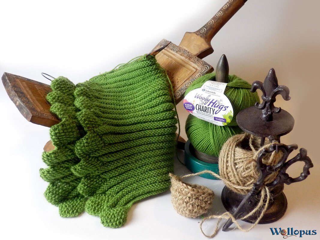 Halbfertiger Rippen-Kragenschal in Grün mit Zierkante, daneben Garnknäuel, Bindfaden und Strickzubehör