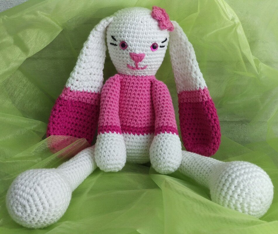 Weiß-rosa Amigurumi-Häschen mit Schlappohren auf grünem Stoff