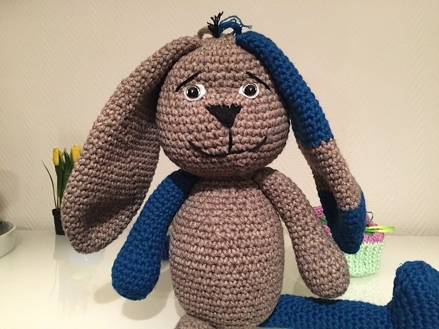 Gehäkelter Amigurumi-Hase in Braun mit blauen Akzenten an Ohr, Arm und Bein.