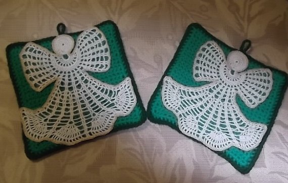 Pair of green crocheted square potholders each with a white crochet angel appliqué, dark green border, and hanging loop, laid on light fabric