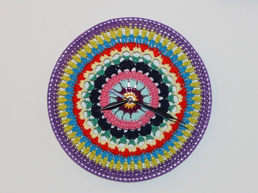 Runde Wanduhr mit buntem gehäkeltem Mandala und schwarzen Uhrzeigern
