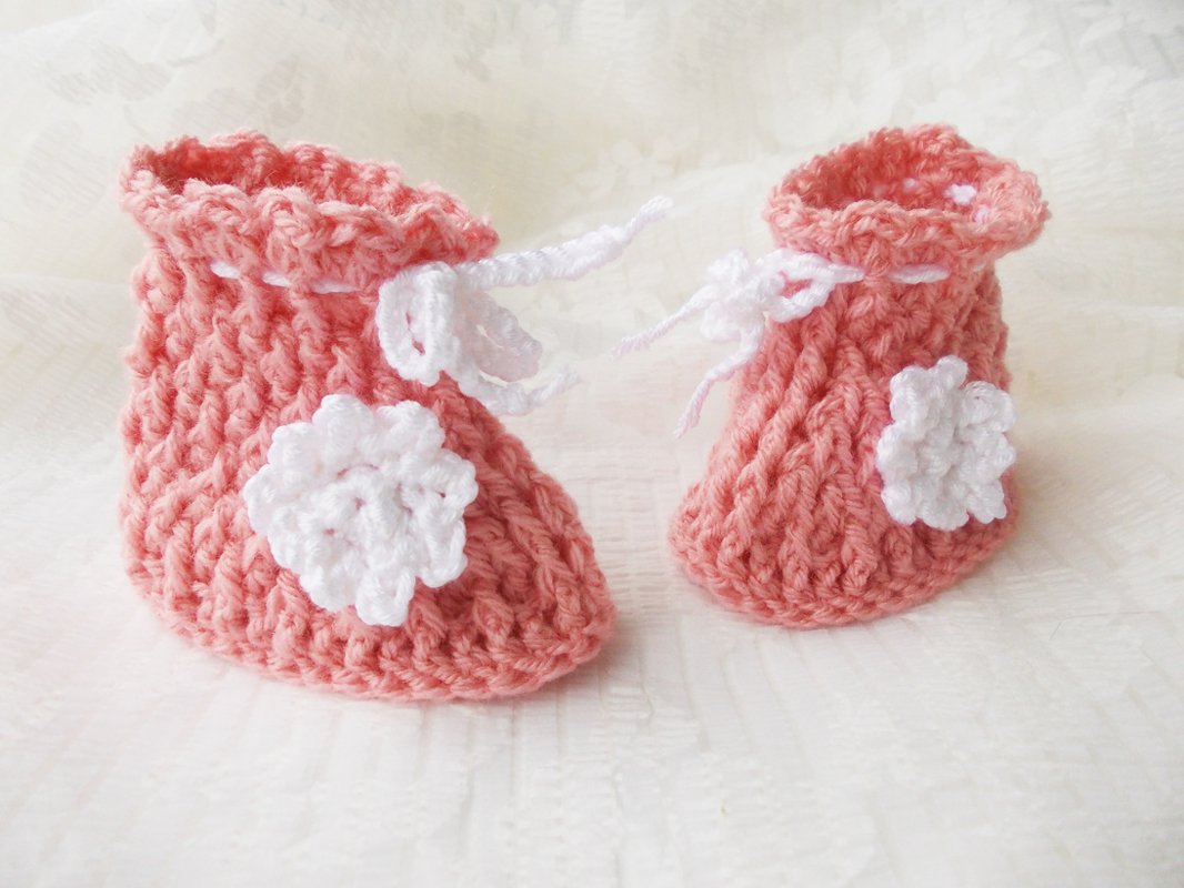 Paar rosa gehäkelte Babyschuhe mit weißen Blumen und weißem Bindeband
