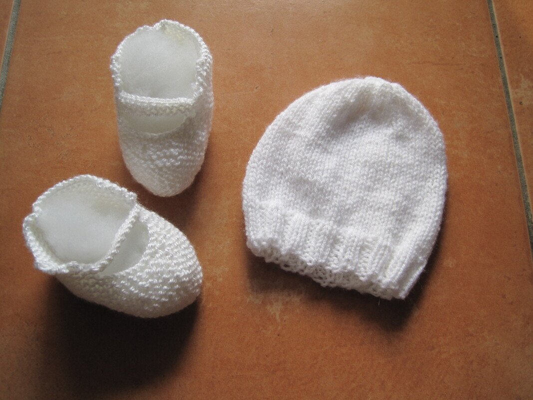 Weißes gestricktes Baby-Set mit Mütze und zwei Schühchen