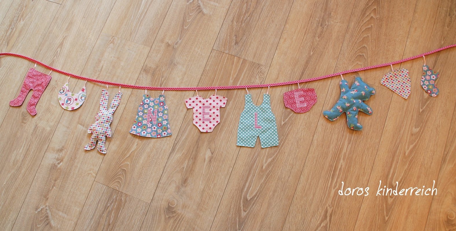 Nähprojekt Girlande aus Reststoffen mit verschiedenen Babykleidungsformen an einer Kordel