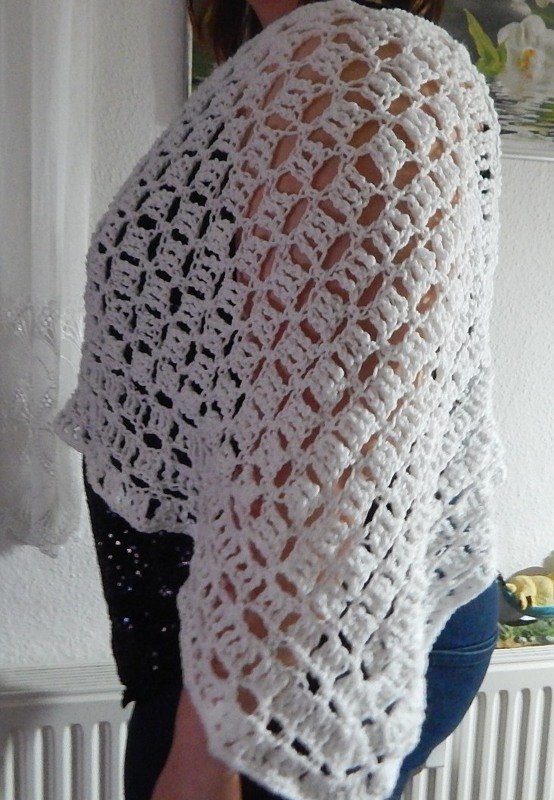 Person trägt weißen, locker gehäkelten Poncho mit offenem Lochmuster, seitliche Ansicht