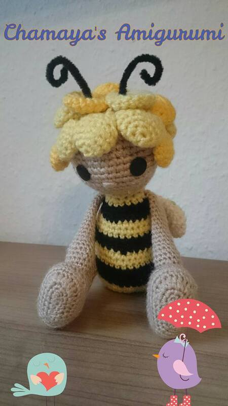 Gehäkelte Amigurumi-Biene mit gelbem Haarschopf und gestreiftem Körper auf Holzuntergrund