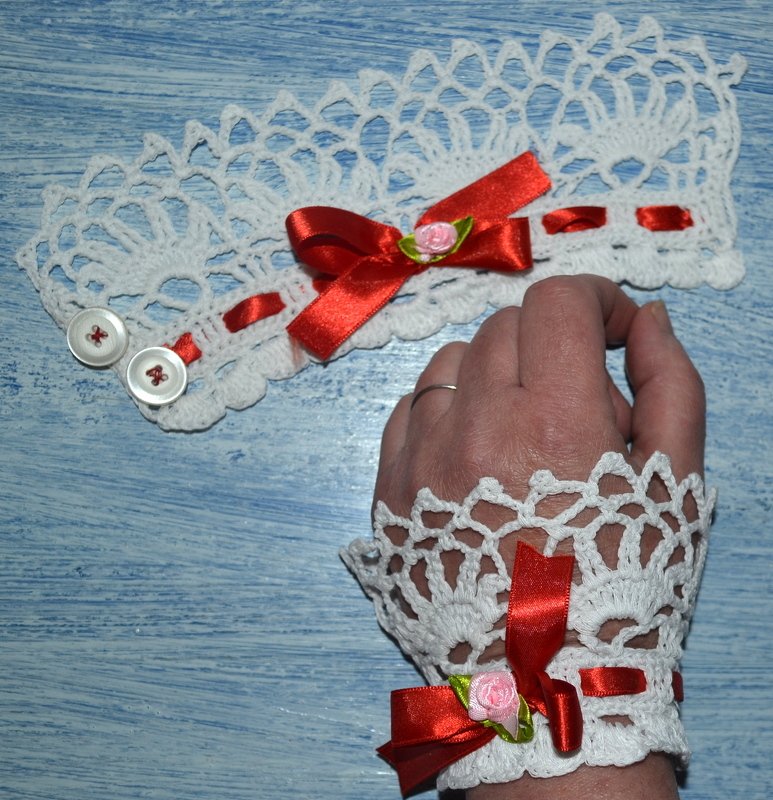 Weiße gehäkelte Armstulpe mit roter Satinschleife und Rosenapplikation am Handgelenk