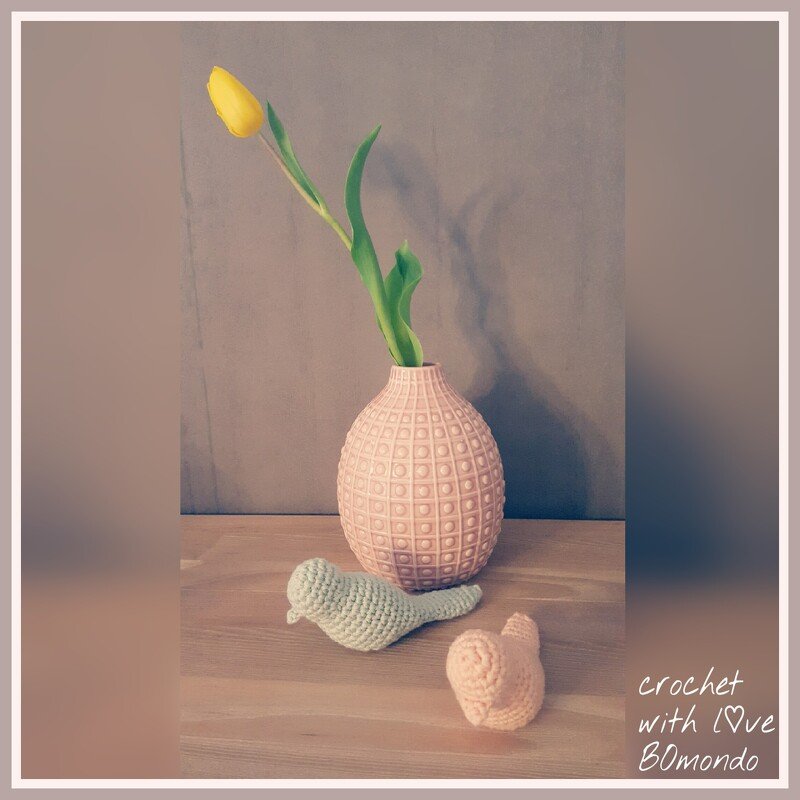 Kleine gehäkelte Vögel in Pastell neben rosa Vase mit gelber Tulpe