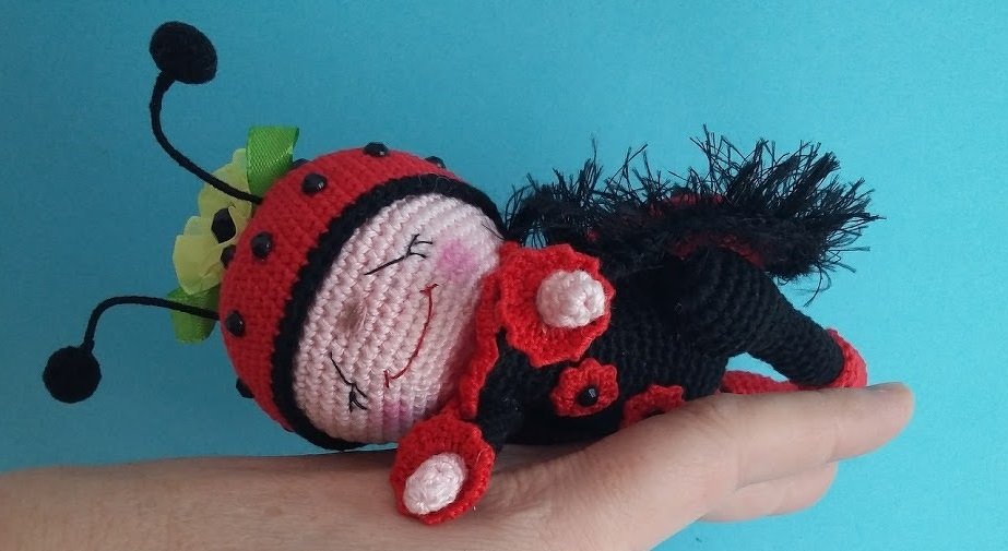Hand hält kleines gehäkeltes Marienkäfer-Amigurumi in Rot und Schwarz mit lächelndem Gesicht