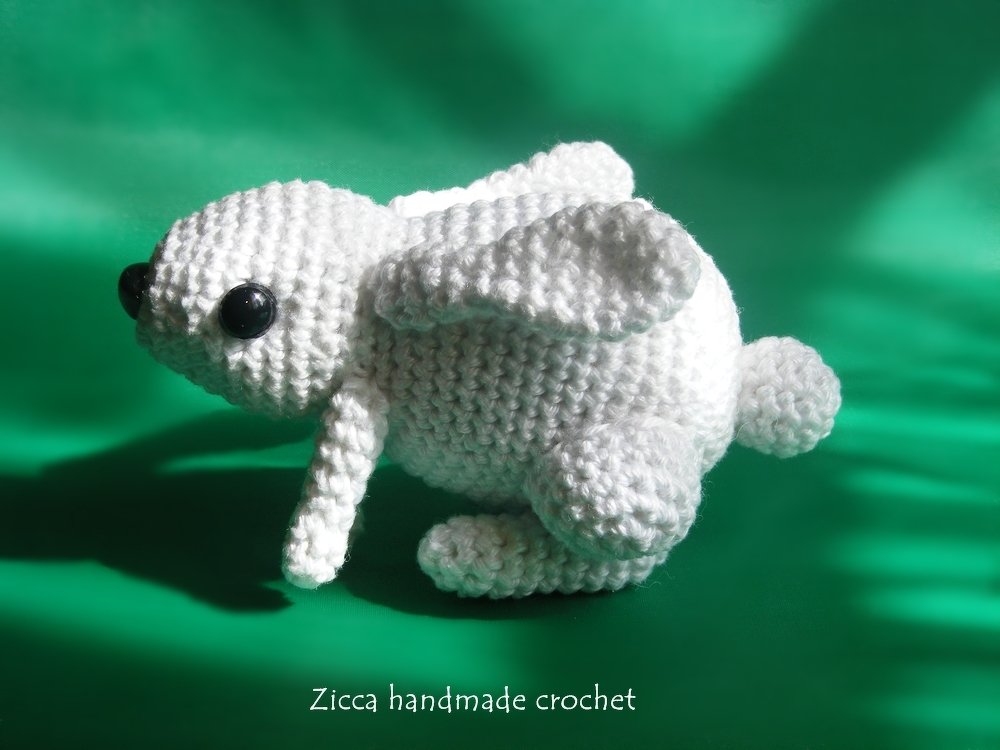 White crocheted amigurumi rabbit with black safety eyes on a green background.