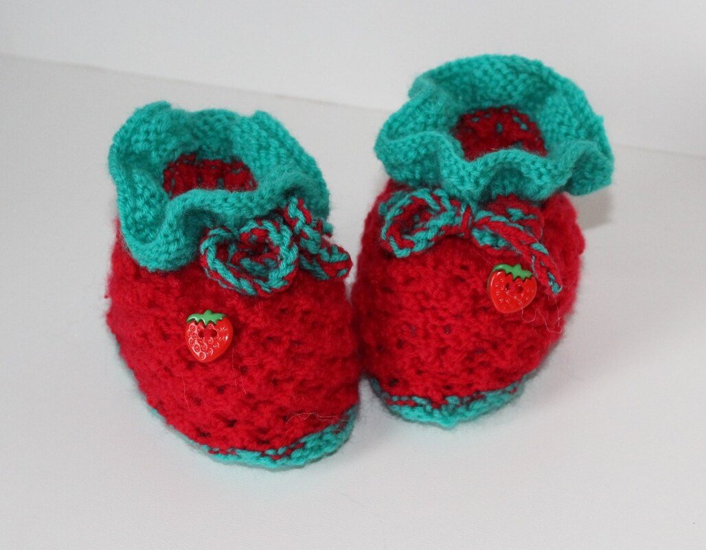 Rote gestrickte Babyschuhe mit türkisfarbener Rüsche und Erdbeerknöpfen