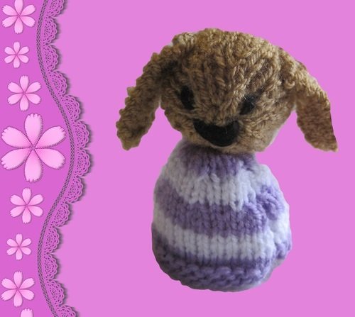 Gestrickter Hasen-Eierwärmer mit braunem Kopf und lila-weiß gestreiftem Körper vor pinkem Hintergrund mit Blumenrand.