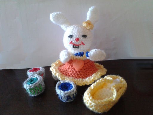 Weißes gehäkeltes Amigurumi-Häschen mit orange-gelbem Kleid, Herz-Applikation, Blume am Ohr und kleinen gehäkelten Accessoires