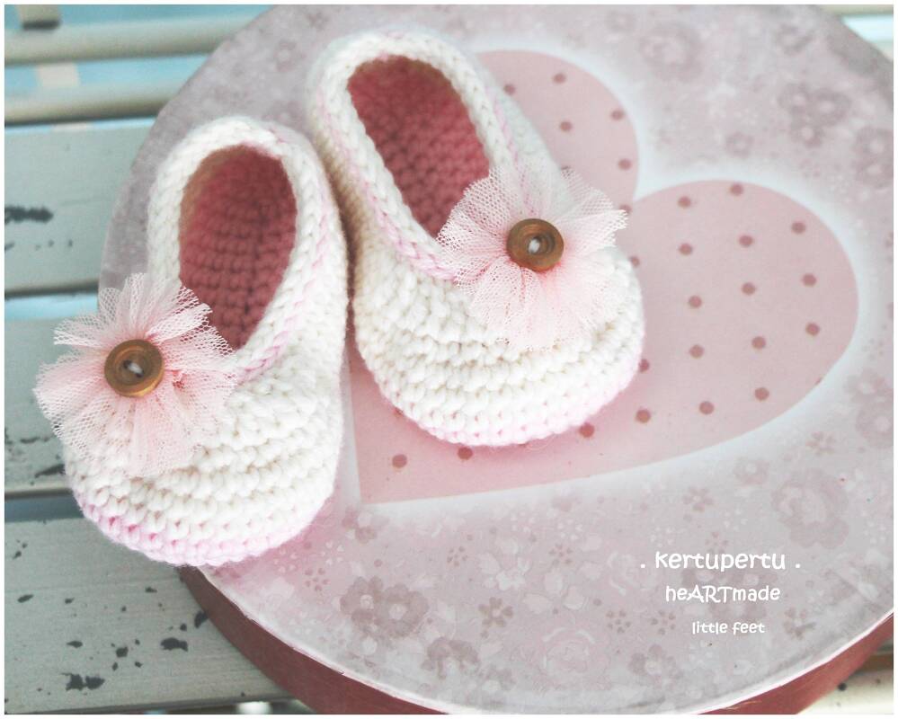 Gehäkelte Baby-Ballerinas in Creme und Rosa mit Tüllblüten und Holzknopf auf rosa Herzbox
