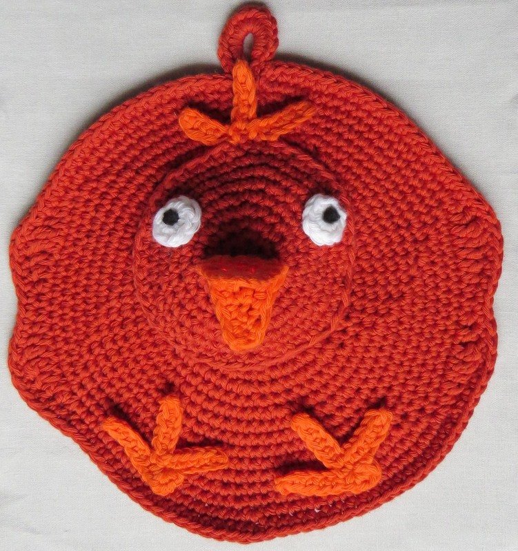 Runder gehäkelter Topflappen in Hühnerform, orange mit weißen Augen und orangenem Schnabel.
