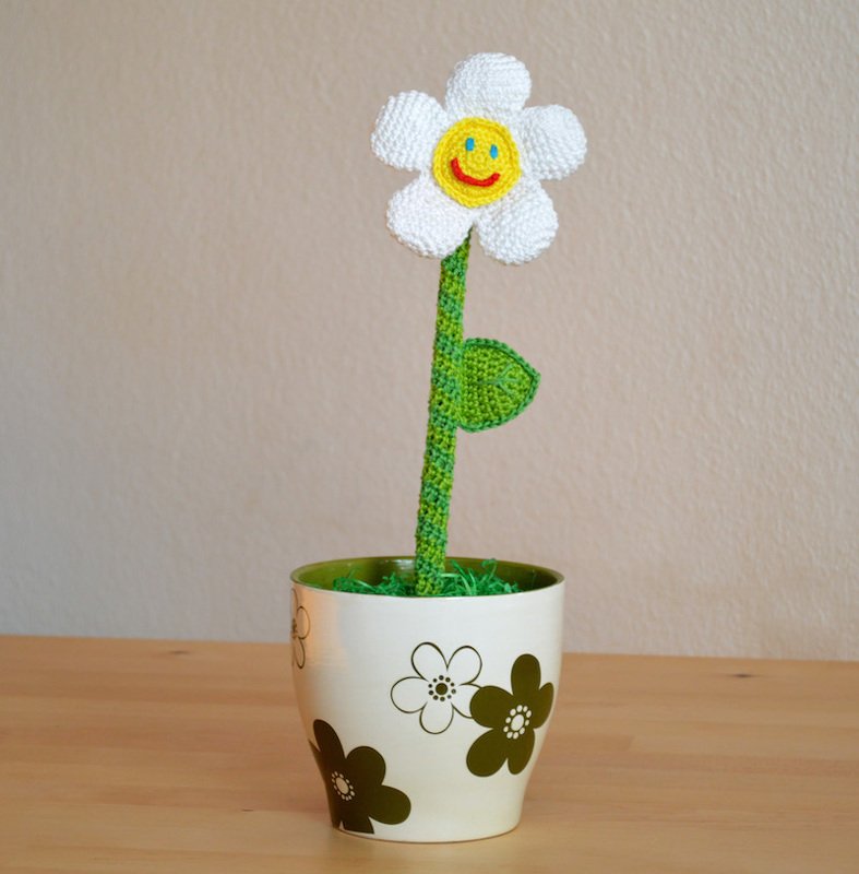 Gehäkelte weiße Margeritenblüte mit gelbem Lächeln in cremefarbenem Topf
