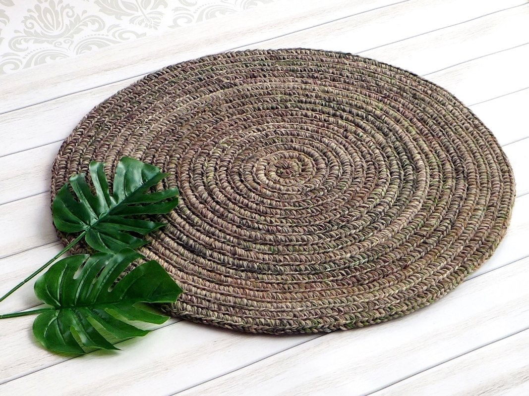 Runder gehäkelter Untersetzer in Erdtönen mit spiralförmigem Muster und zwei Monstera-Blättern auf hellem Holz.