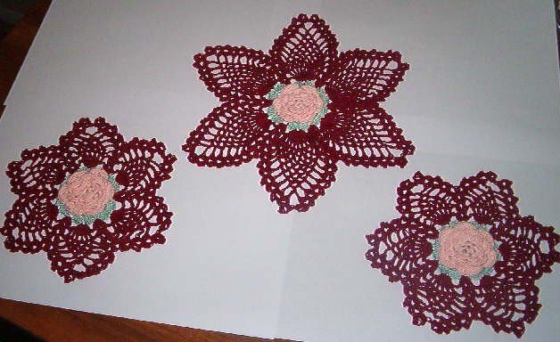 Three burgundy crochet flower doilies with pink and green centers on white