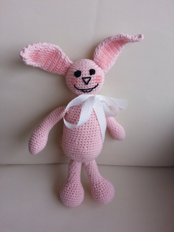 Rosa gehäkelter Hase mit weißer Schleife, langen Ohren und gesticktem Gesicht