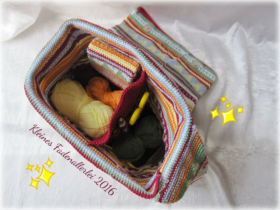 Draufsicht auf eine gestreifte, gehäkelte Umhängetasche mit Innentaschen, Garnknäueln und Häkelnadeln