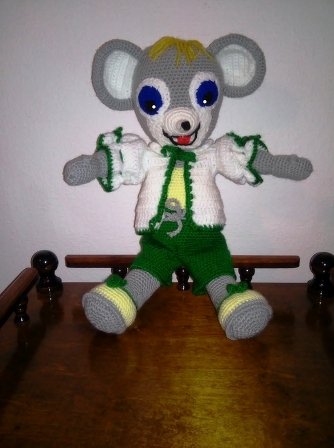 Gehäkelte graue Amigurumi‑Maus sitzend mit weißer Jacke und grüner Hose