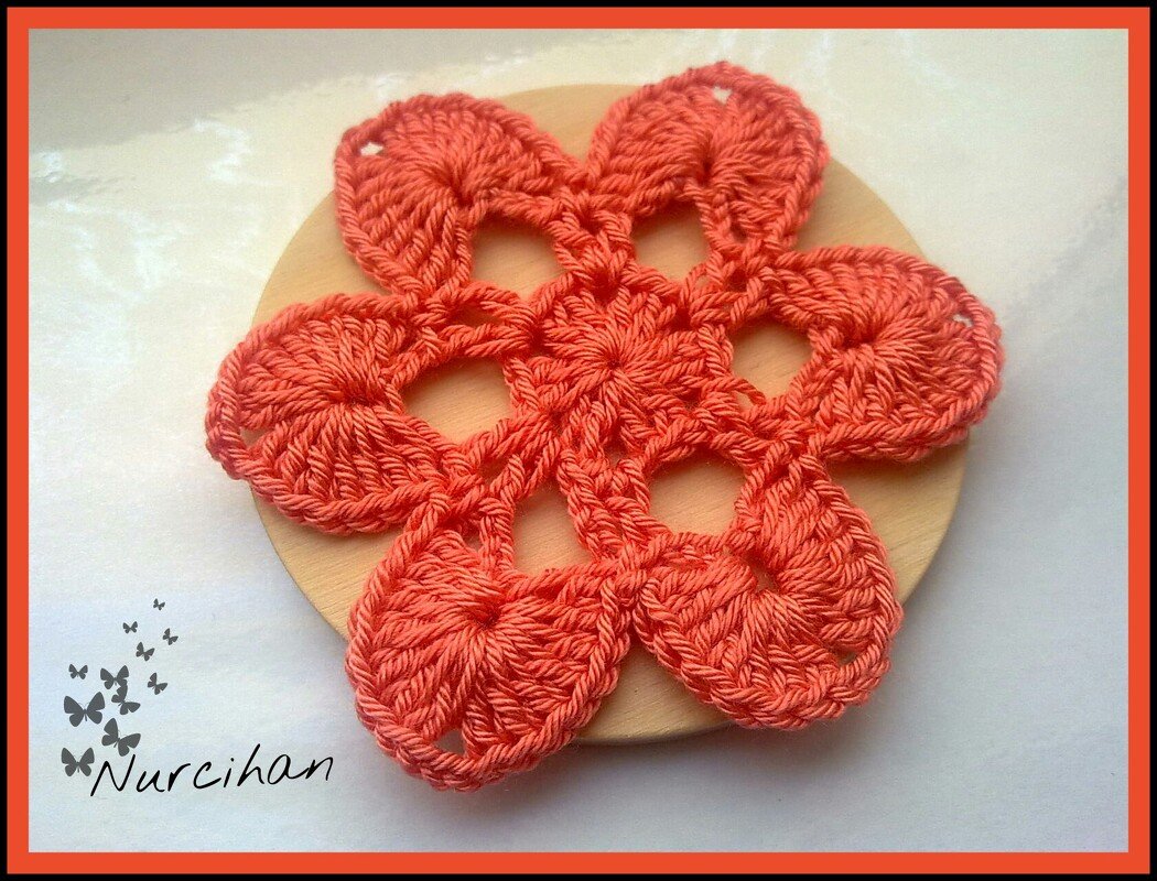 Lachsfarbener gehäkelter Untersetzer in Blumenform mit sechs Blütenblättern auf hellem Holzhintergrund.